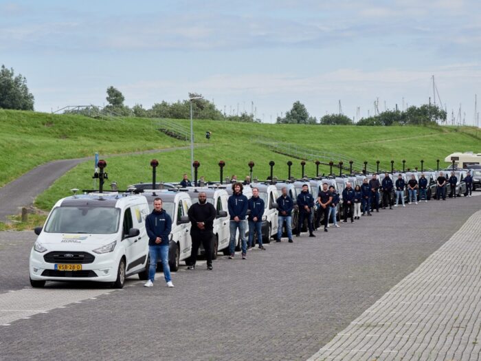People standing in front of a line of identical white vans with roof-mounted cameras