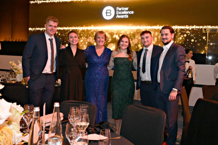 Six people in formal attire pose together at a round table during the Partner Excellence Awards event.